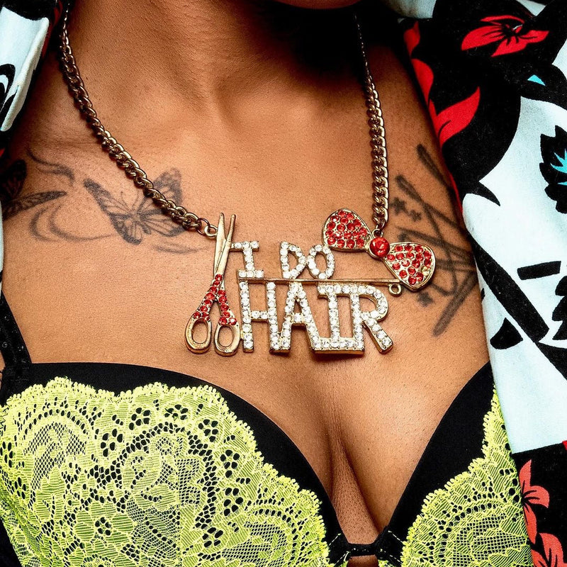 Necklace with 'I Do Hair' pendant worn by a person with tattoos and colorful clothing.